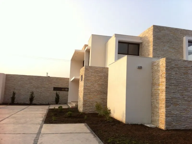 Modern two-story home with white walls and stacked stone accents. Concrete driveway and minimal landscaping.