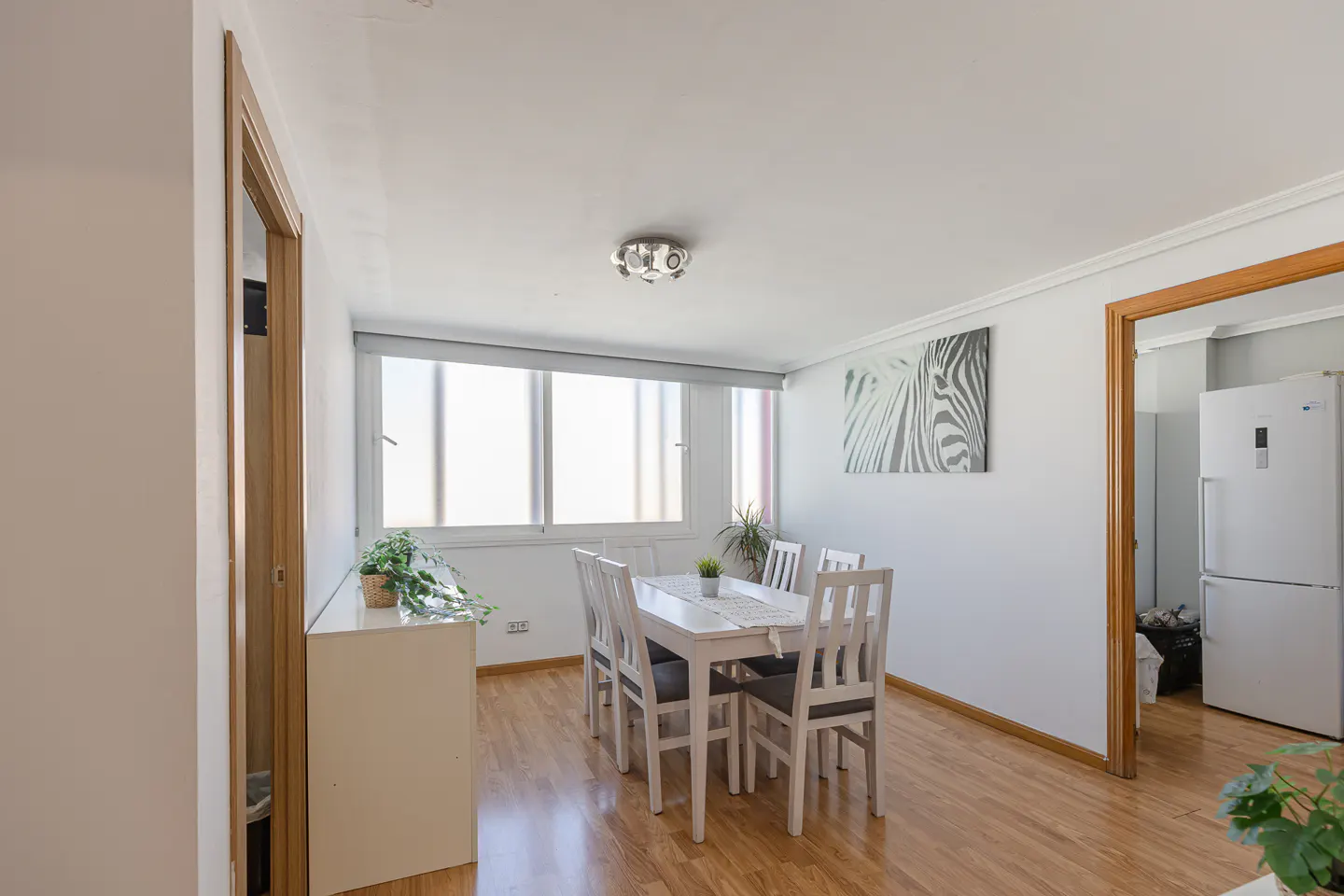 Bright dining room with wood floors, white walls, and a white table with six chairs. A zebra print hangs on the wall.