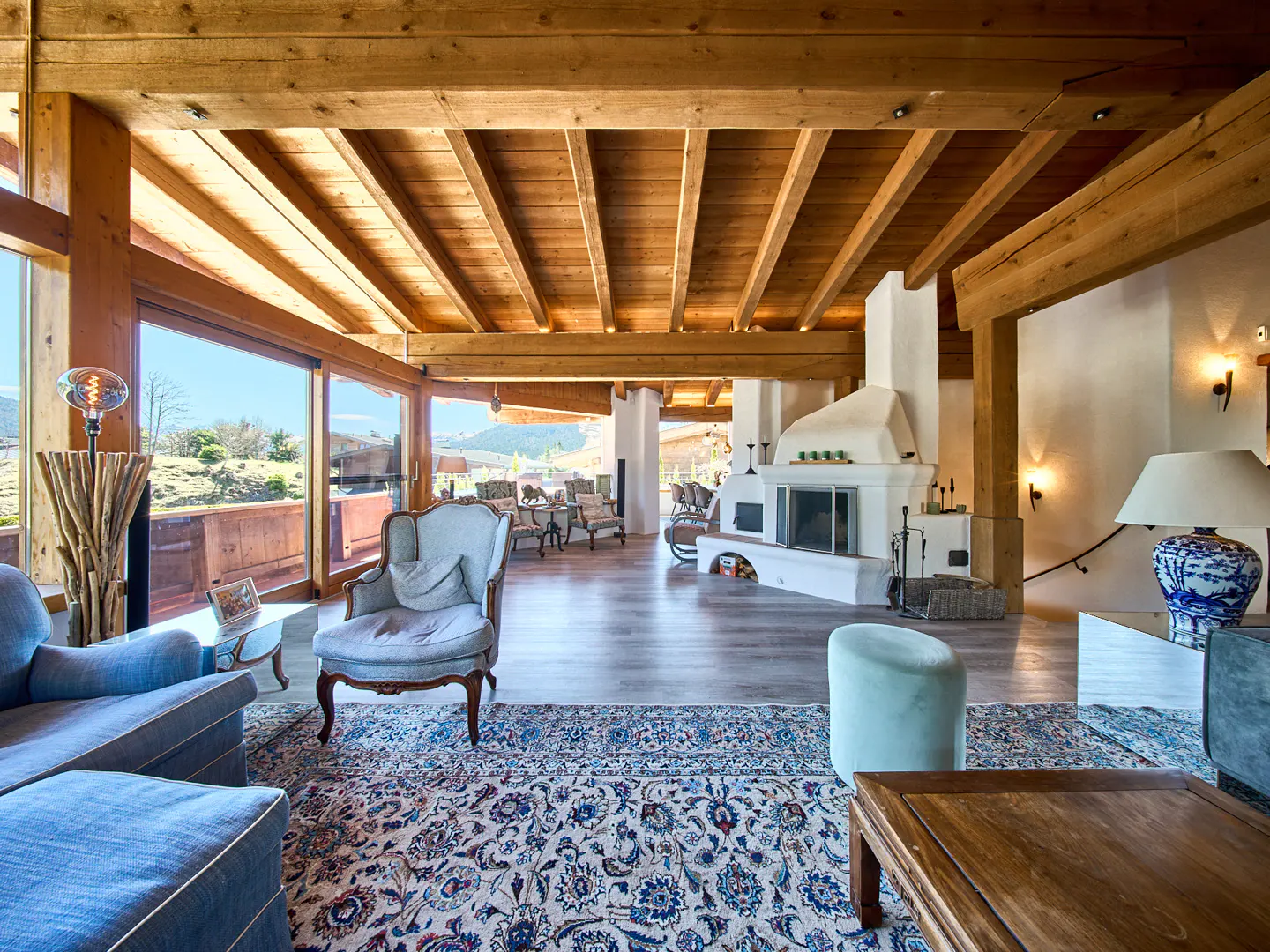 Living room with wood-beamed ceiling, blue furniture, fireplace, and large windows with a view.