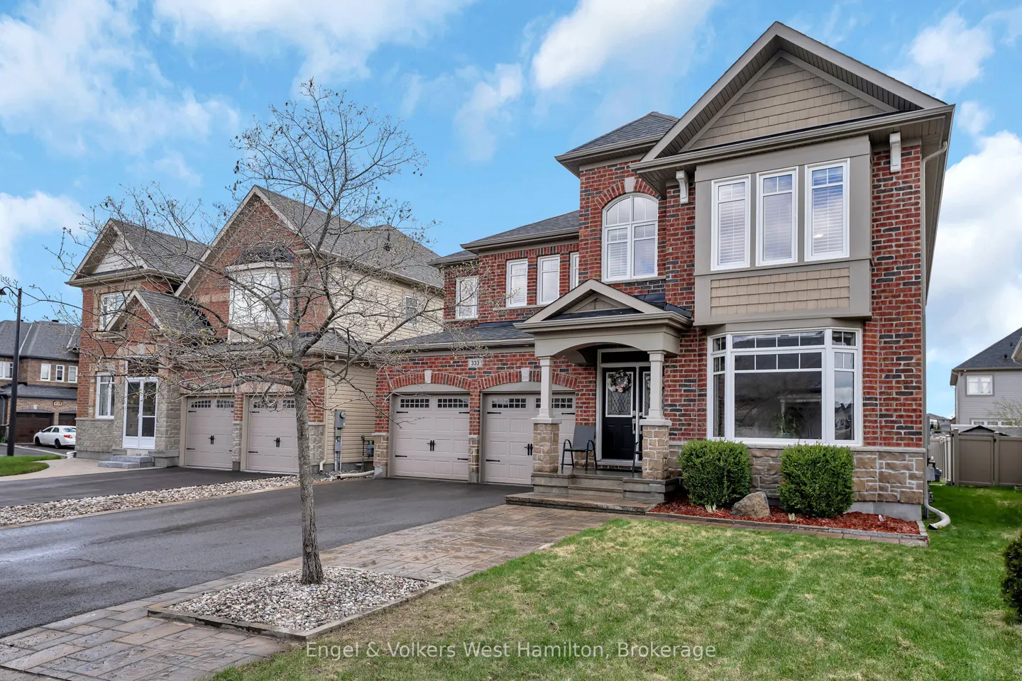 Exterior view of a two-story brick house with a two-car garage and a well-manicured lawn on a sunny day.