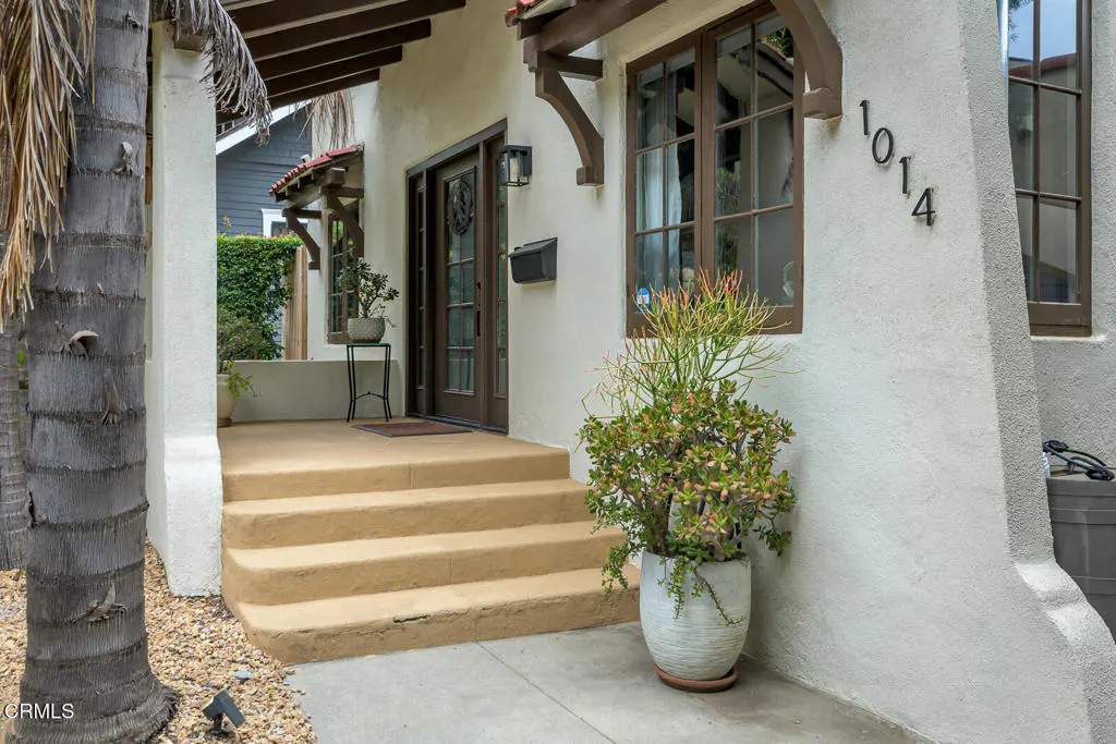 Exterior view of a stucco house with brown trim, steps leading to the front door, and a potted plant. The house number "1014" is visible.