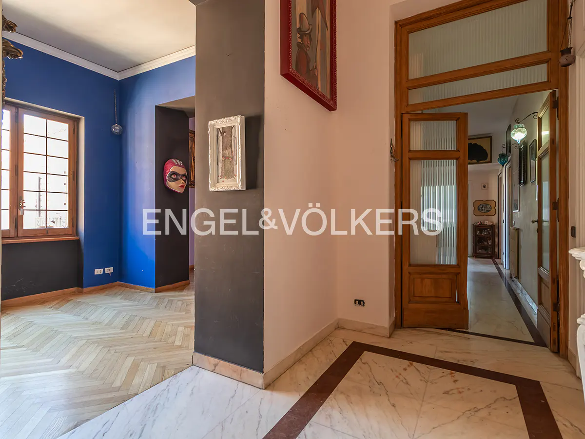 Interior view of a home with marble floors, wooden doors, and blue walls. Artwork and a mask adorn the walls.