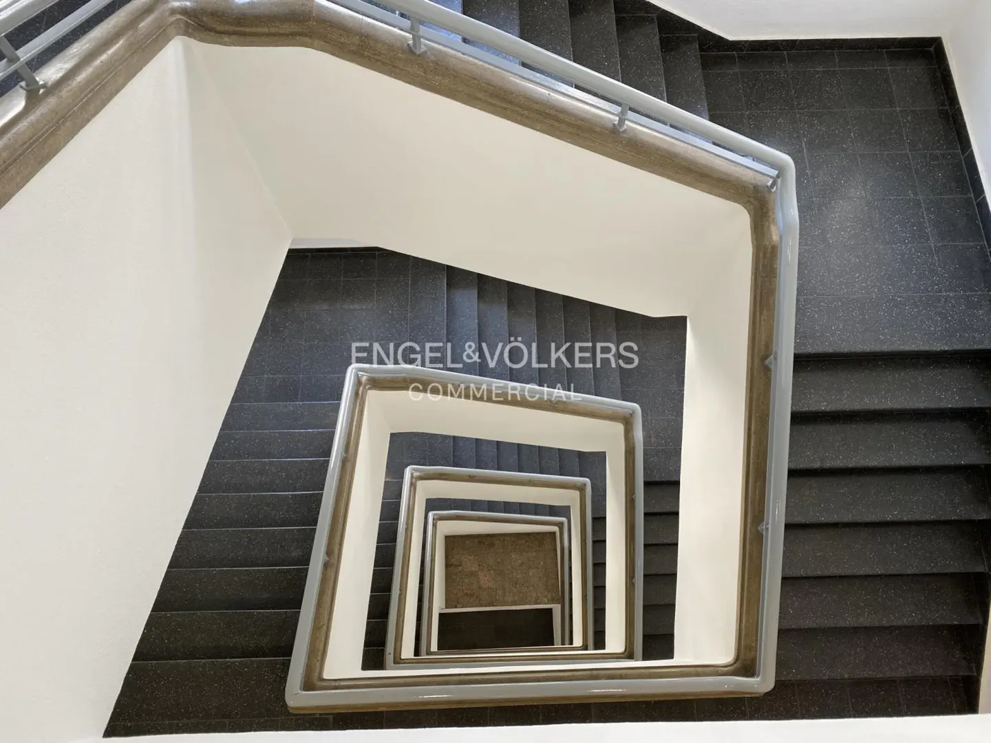 Looking down a square staircase with black steps and white walls. Engel & Völkers logo is visible.