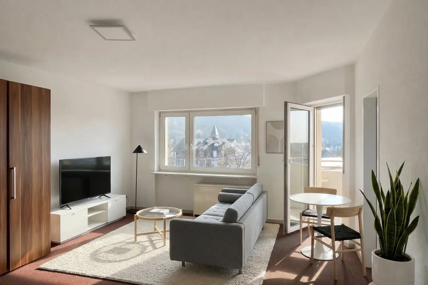 Modern living room with a grey sofa, white media console, round dining table, and a balcony door with a scenic view.