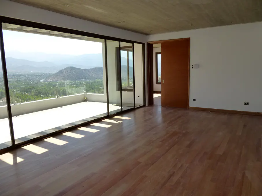 Bright, empty room with wood floors, white walls, and a sliding wood door. Large glass doors open to a balcony with a mountain view.