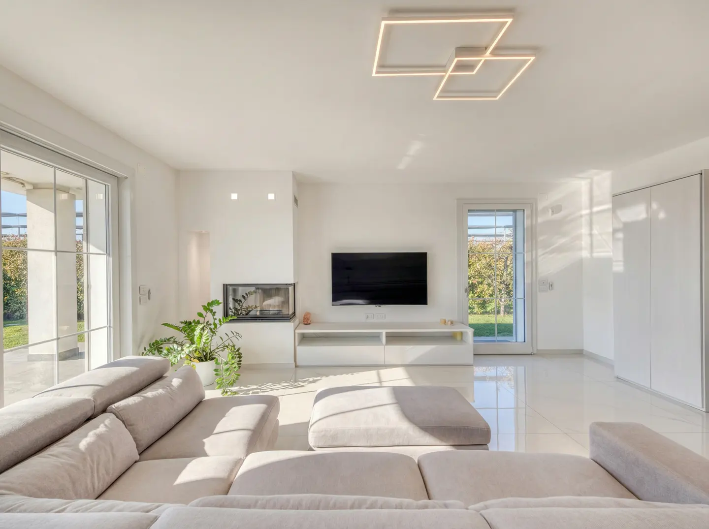 Bright living room with a beige sectional sofa, white walls, tile floor, fireplace, and a flat screen TV. Square LED ceiling light.