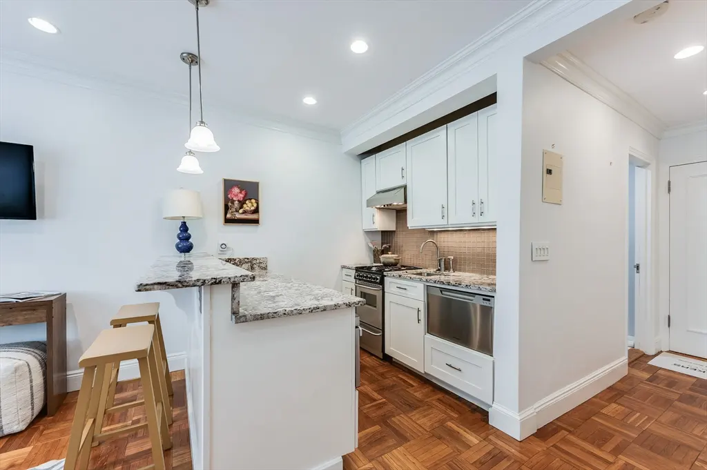 Bright kitchen with white cabinets, granite countertops, and wood floors. Two stools sit at the breakfast bar.