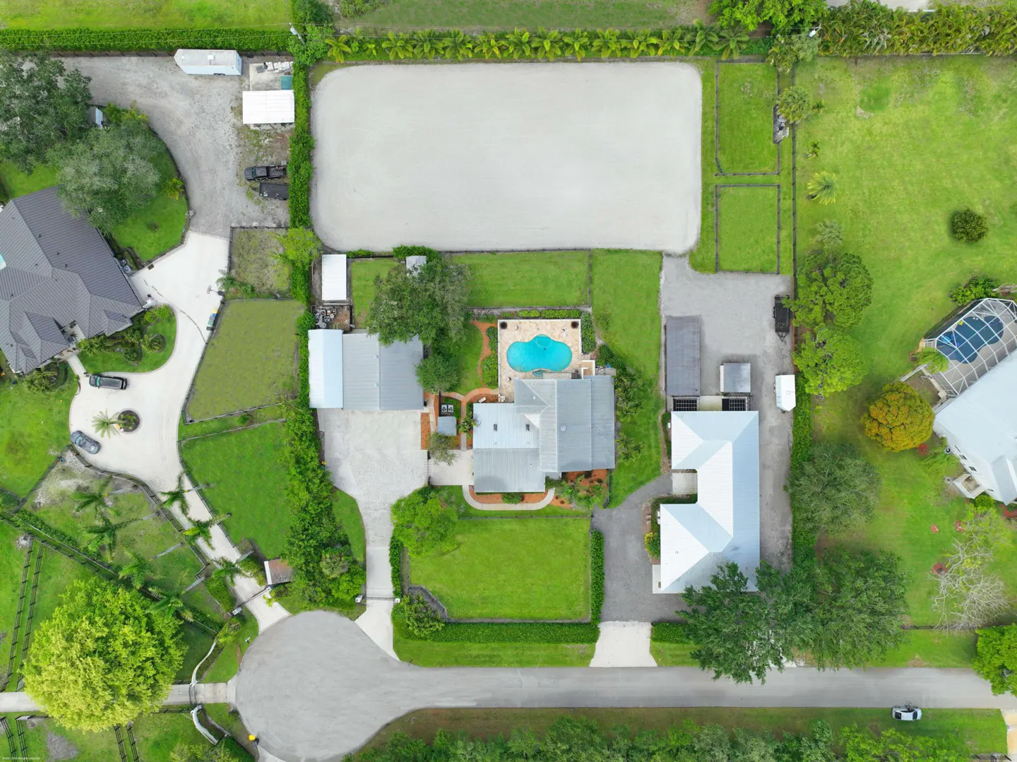 Aerial view of a property with a house, pool, horse arena, and green lawns.