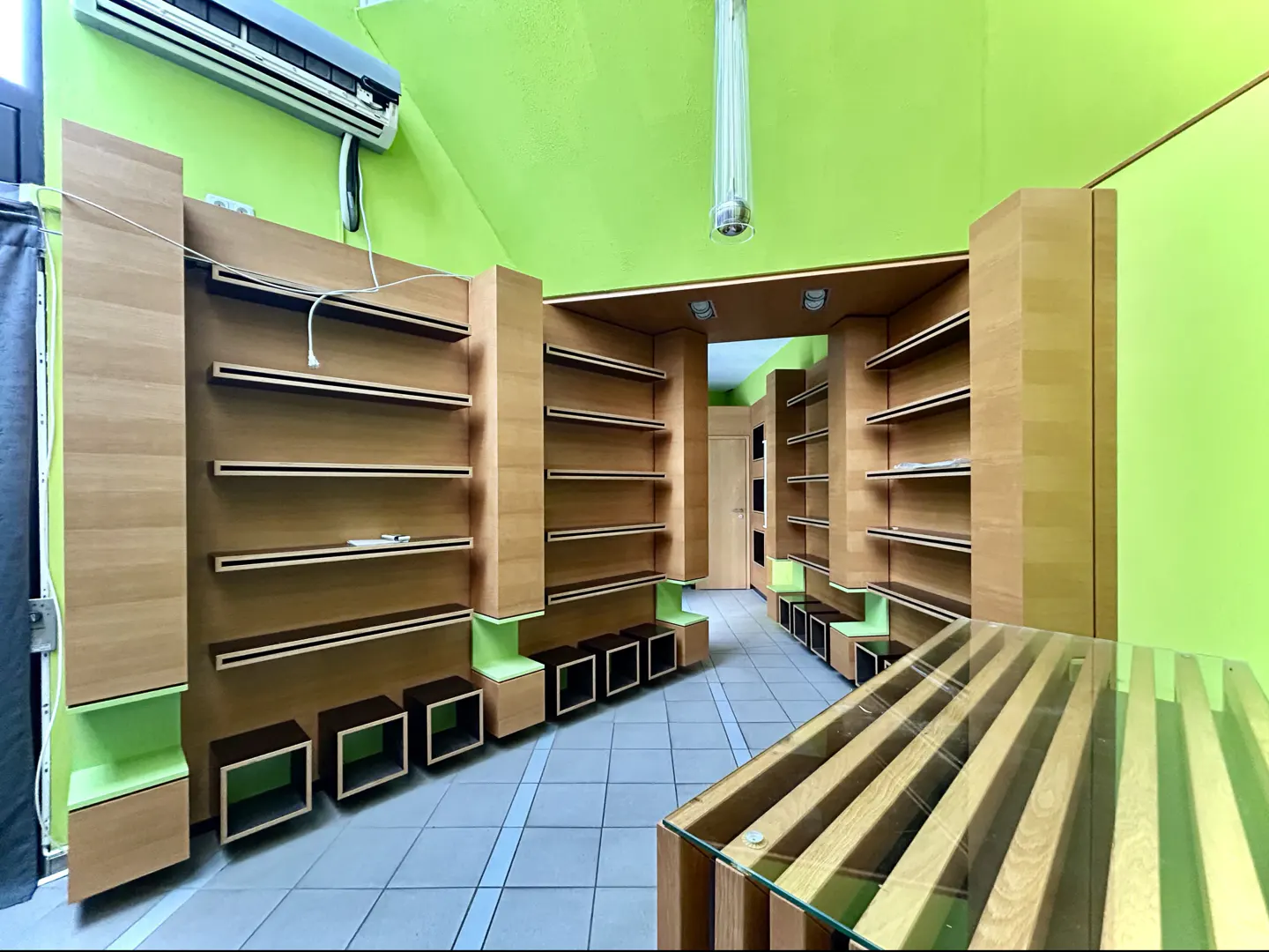 Interior of a retail space with light wood shelving, green walls, and a glass-topped display table.