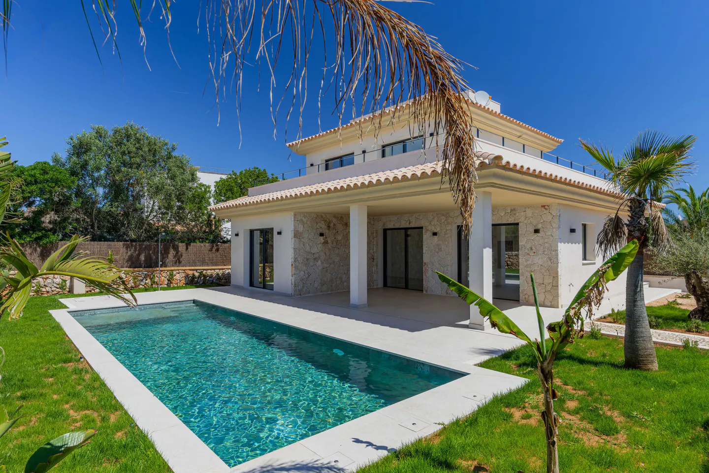 A modern, two-story white house with a pool and green lawn under a clear blue sky.
