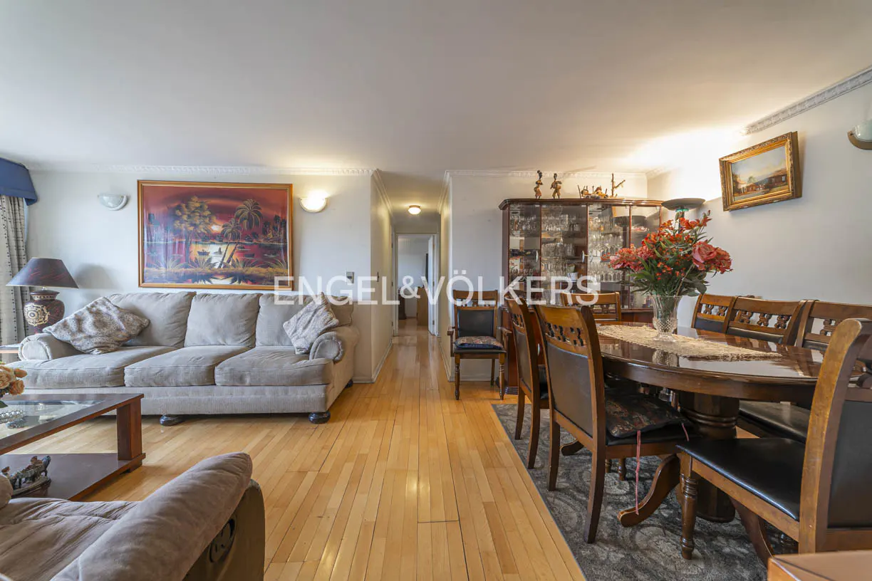 A wide shot of a living and dining room with hardwood floors, a beige sofa, and a dark wood dining table with chairs.