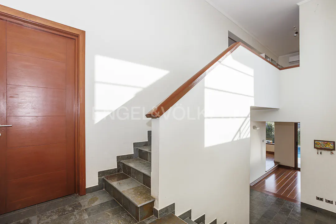 Interior view of a home featuring a wooden door, stone stairs with a wooden handrail, and white walls. A glimpse of a room with wood floors is visible.