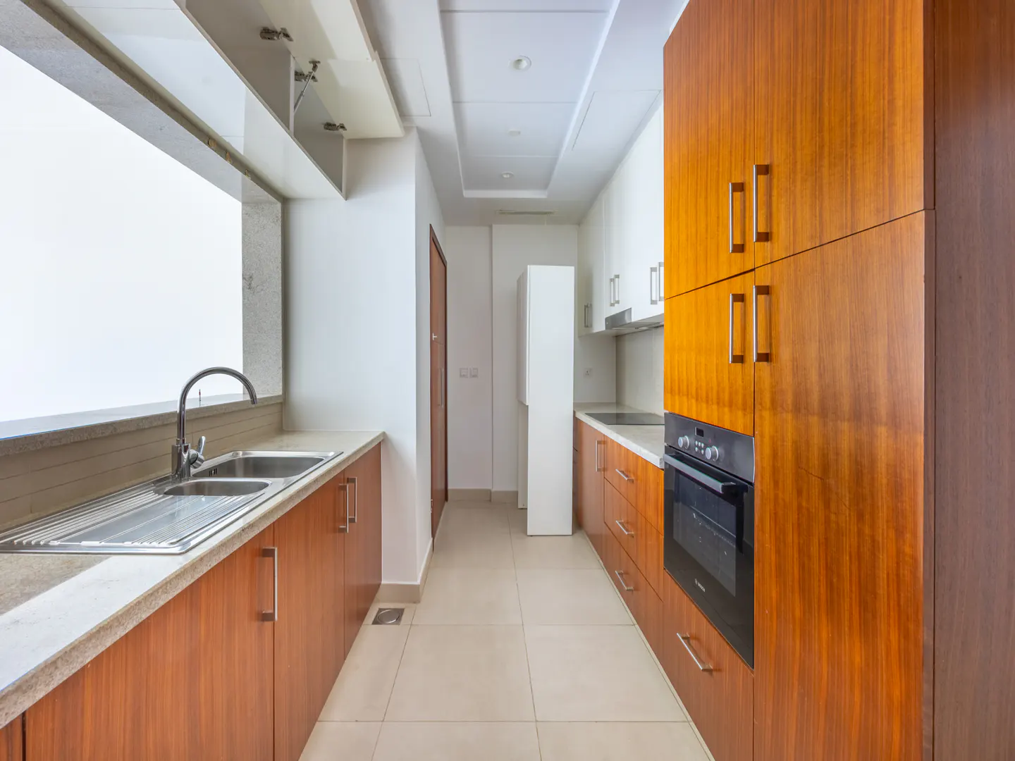 A bright kitchen with wood cabinets, stainless steel sink, and black oven. A window is above the sink.