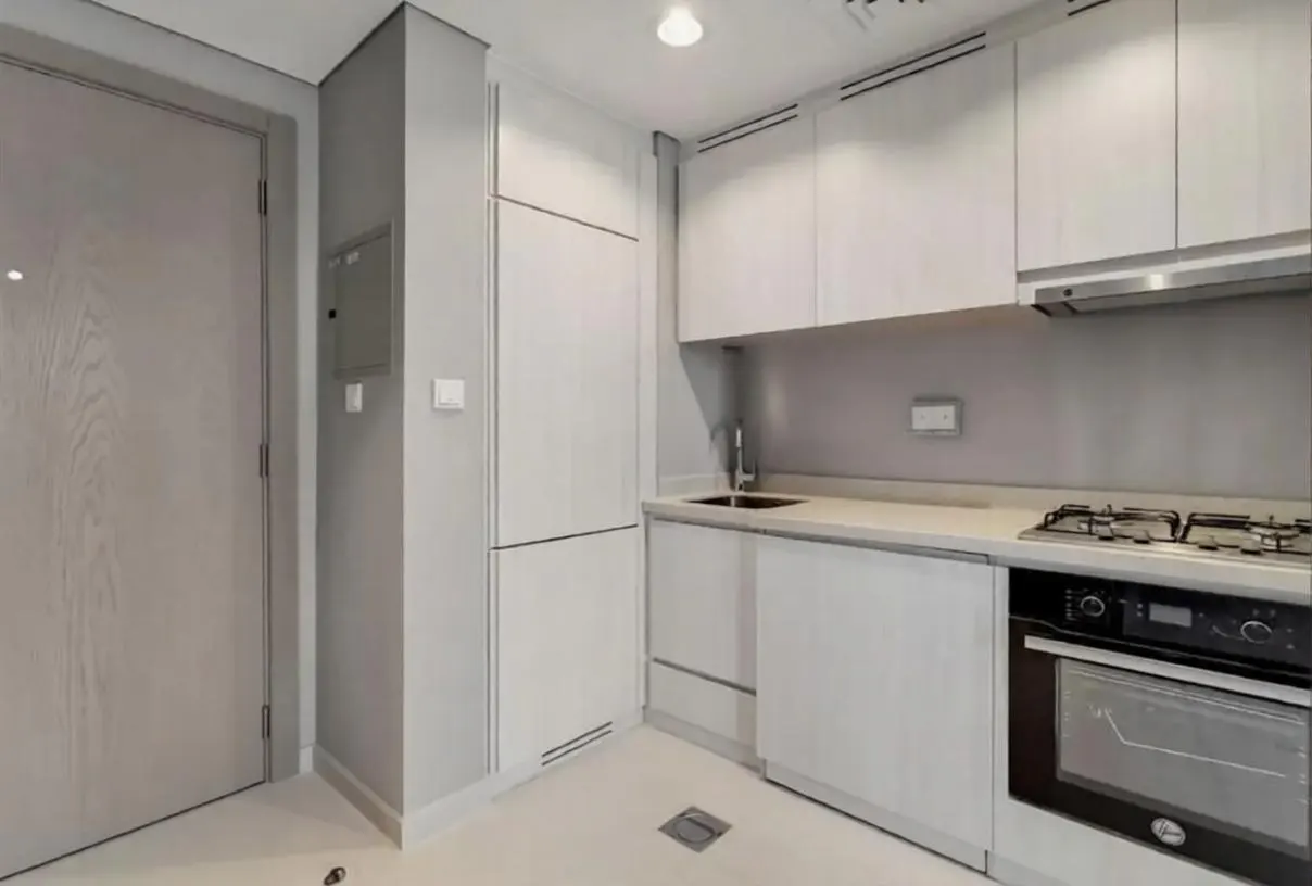A modern kitchen with white cabinets, a stainless steel sink, and a black oven. A light gray door is on the left.