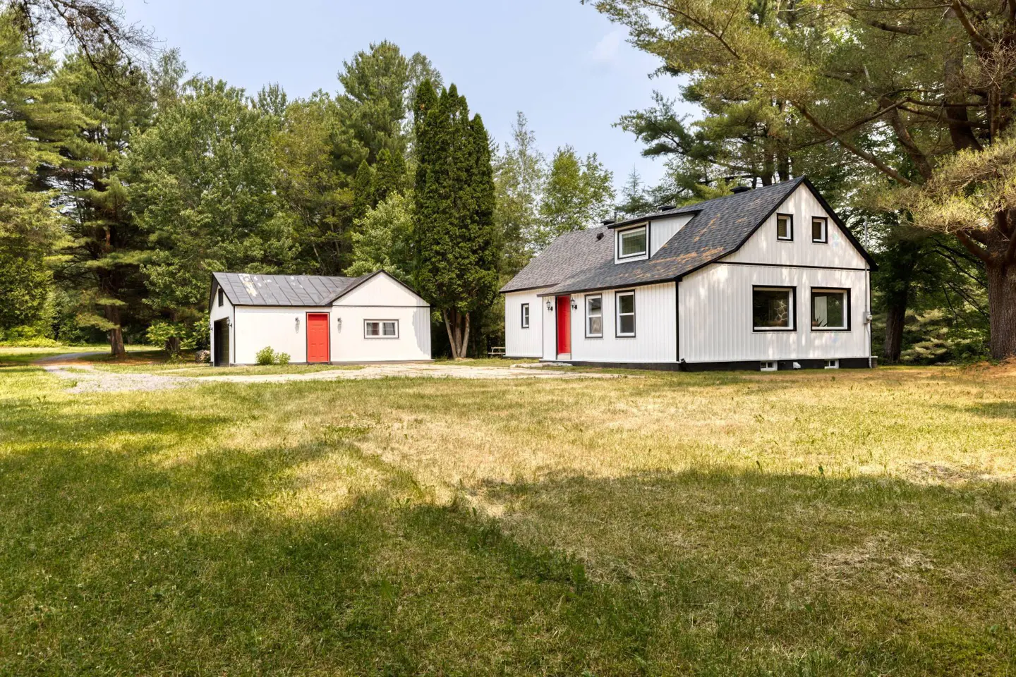 Exterior of a white house with a red door and a detached garage on a grassy lawn.