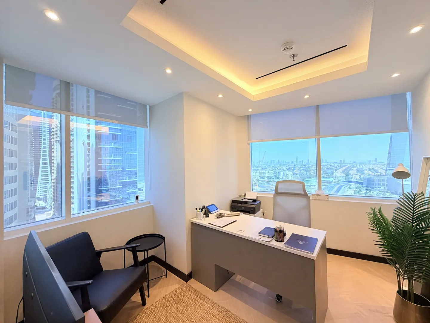 Modern office with a grey desk, black armchair, and large windows offering a panoramic city view.