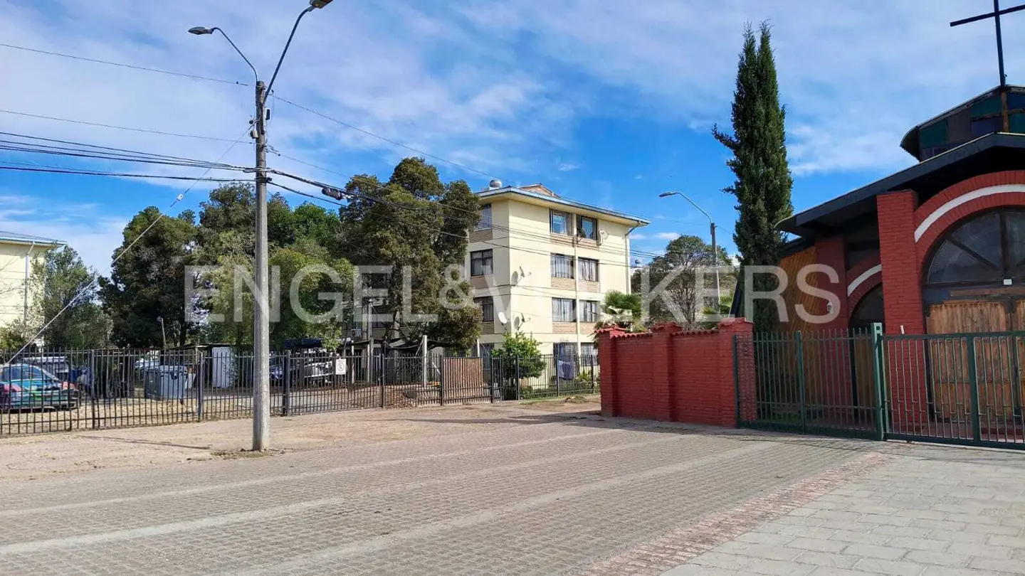 Street view of a three-story apartment building next to a red brick church under a blue sky.