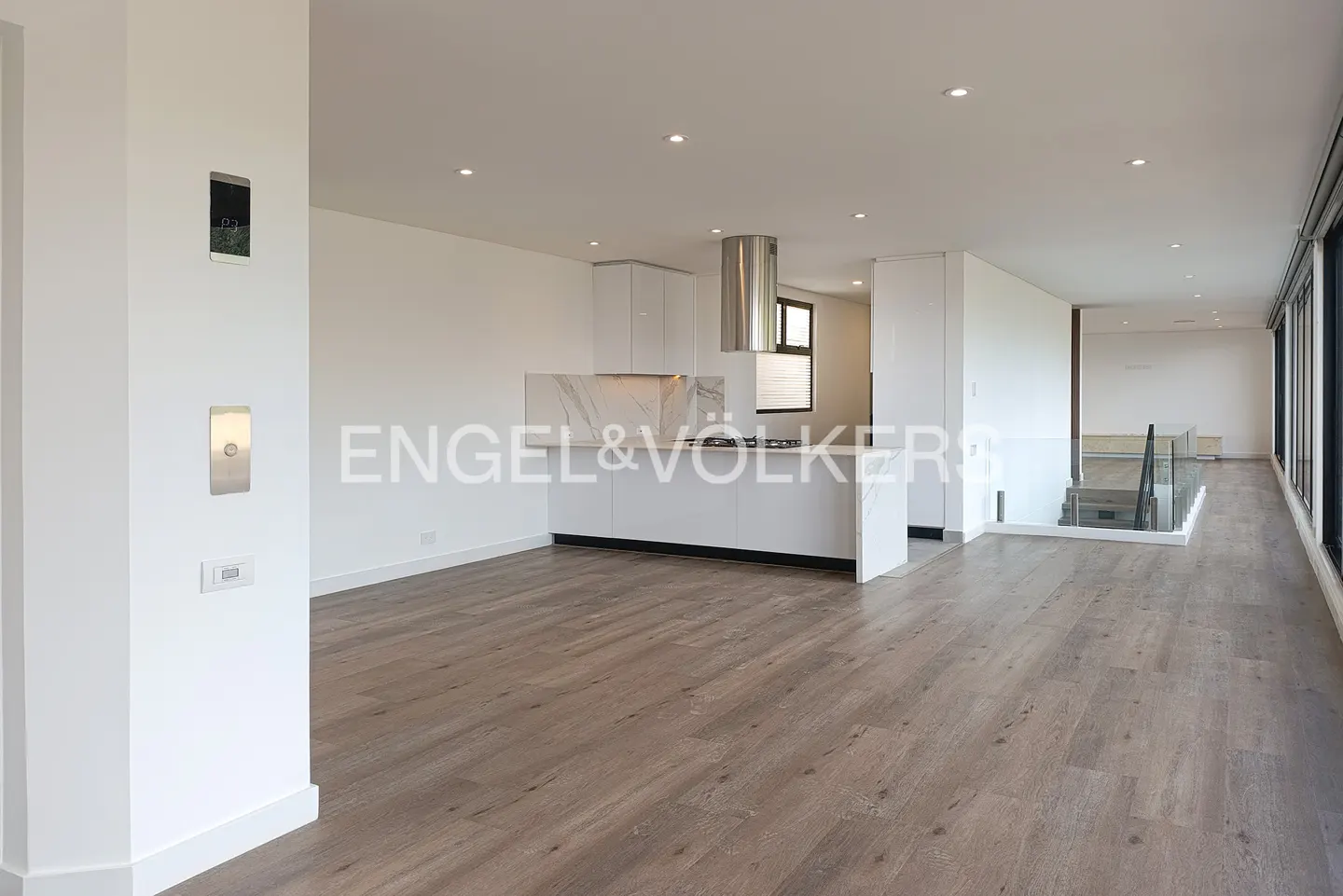 Bright, open-concept apartment with wood floors, white walls, and a modern kitchen with stainless steel appliances. Large windows provide natural light.