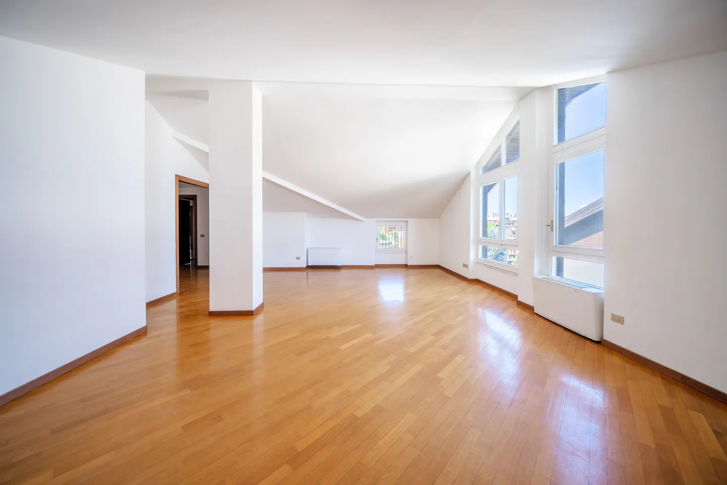 Bright, empty attic apartment with hardwood floors, white walls, and large windows.