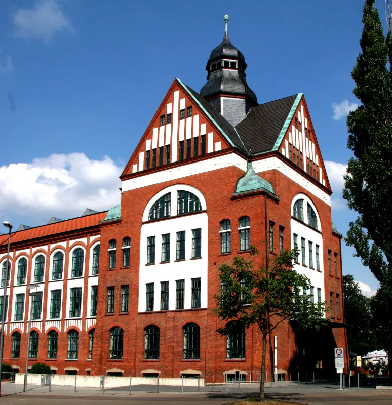 A three-story red brick building with white trim and a black tower against a blue sky.