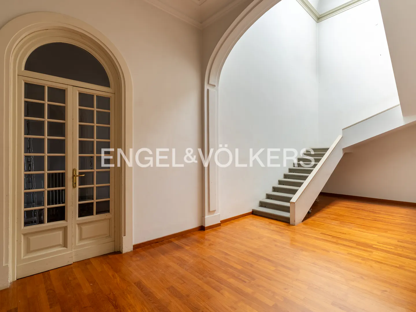 Bright foyer with hardwood floors, an arched glass-paned door, and a staircase leading to an upper level.