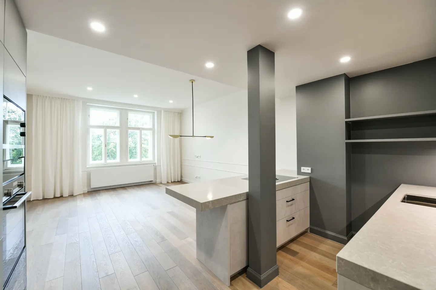 Bright, modern kitchen with gray cabinets, a stone island, and light wood floors. Large windows with white curtains let in natural light.