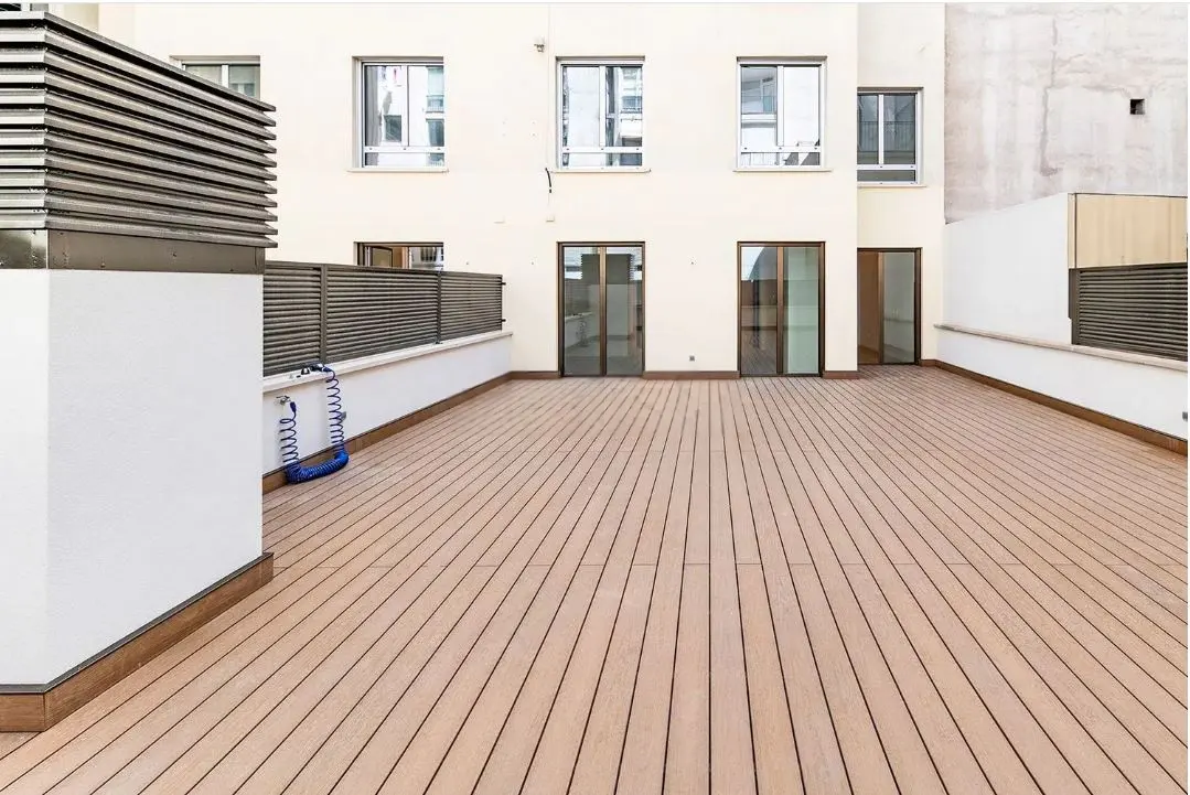 Spacious rooftop terrace with light wood decking, white walls, dark metal railings, and glass doors leading into the home.