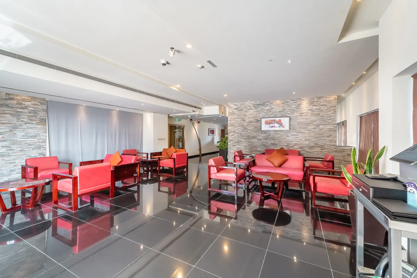 Hotel lobby with red sofas and chairs, dark tile floors, and stone accent walls.