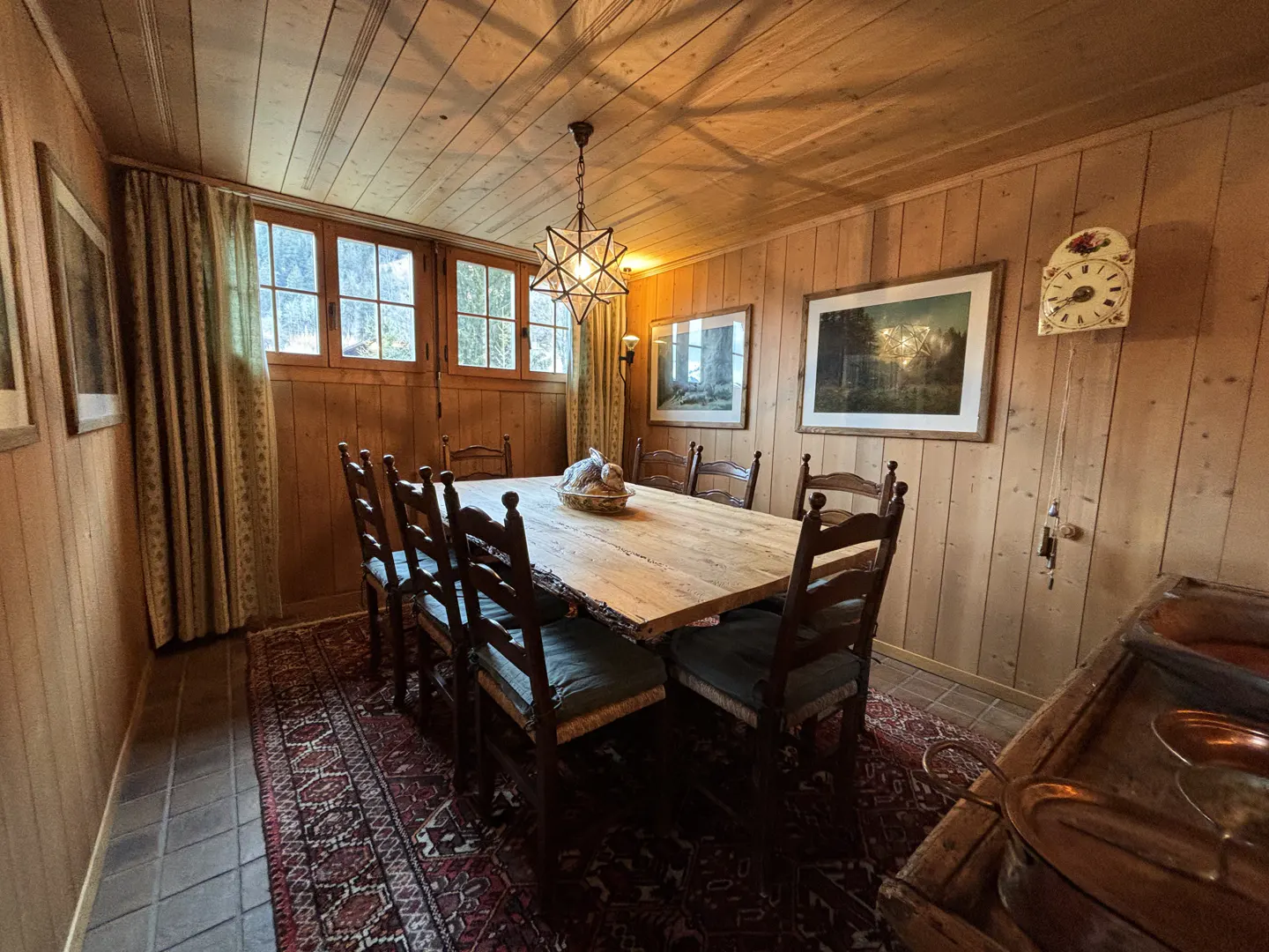 A dining room with wood paneled walls, a long wooden table with chairs, and a star-shaped chandelier.