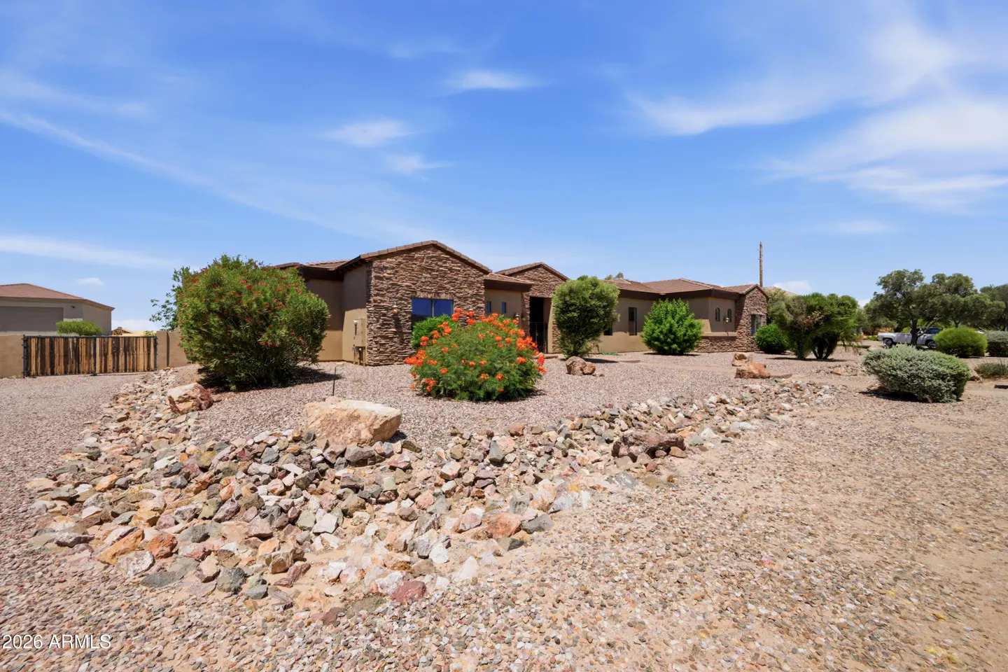 Single-story desert home with stone facade, gravel landscaping, and vibrant orange flowering bushes under a blue sky.