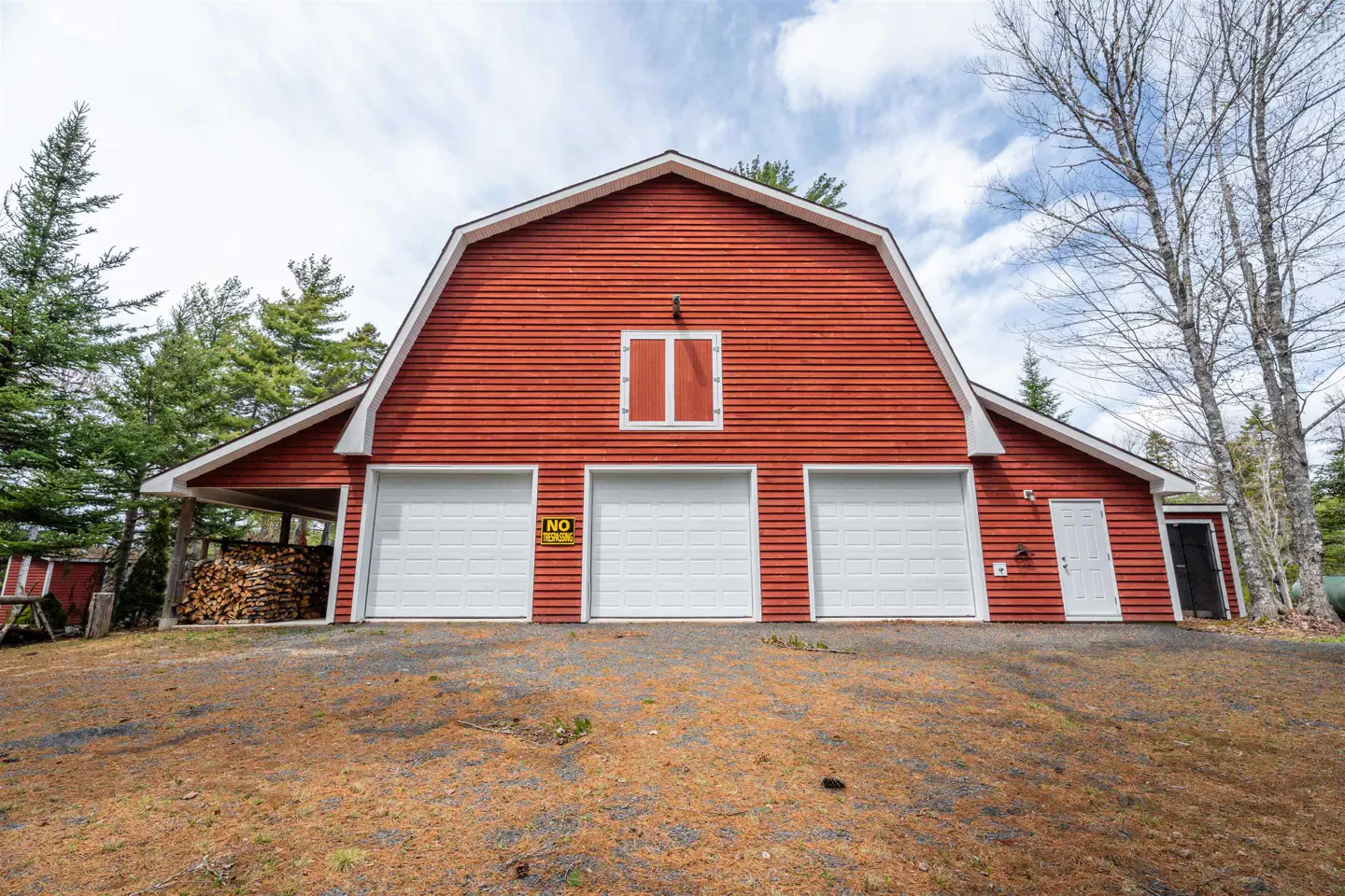 Red barn with three white garage doors and a white door on the right side. Trees in the background.