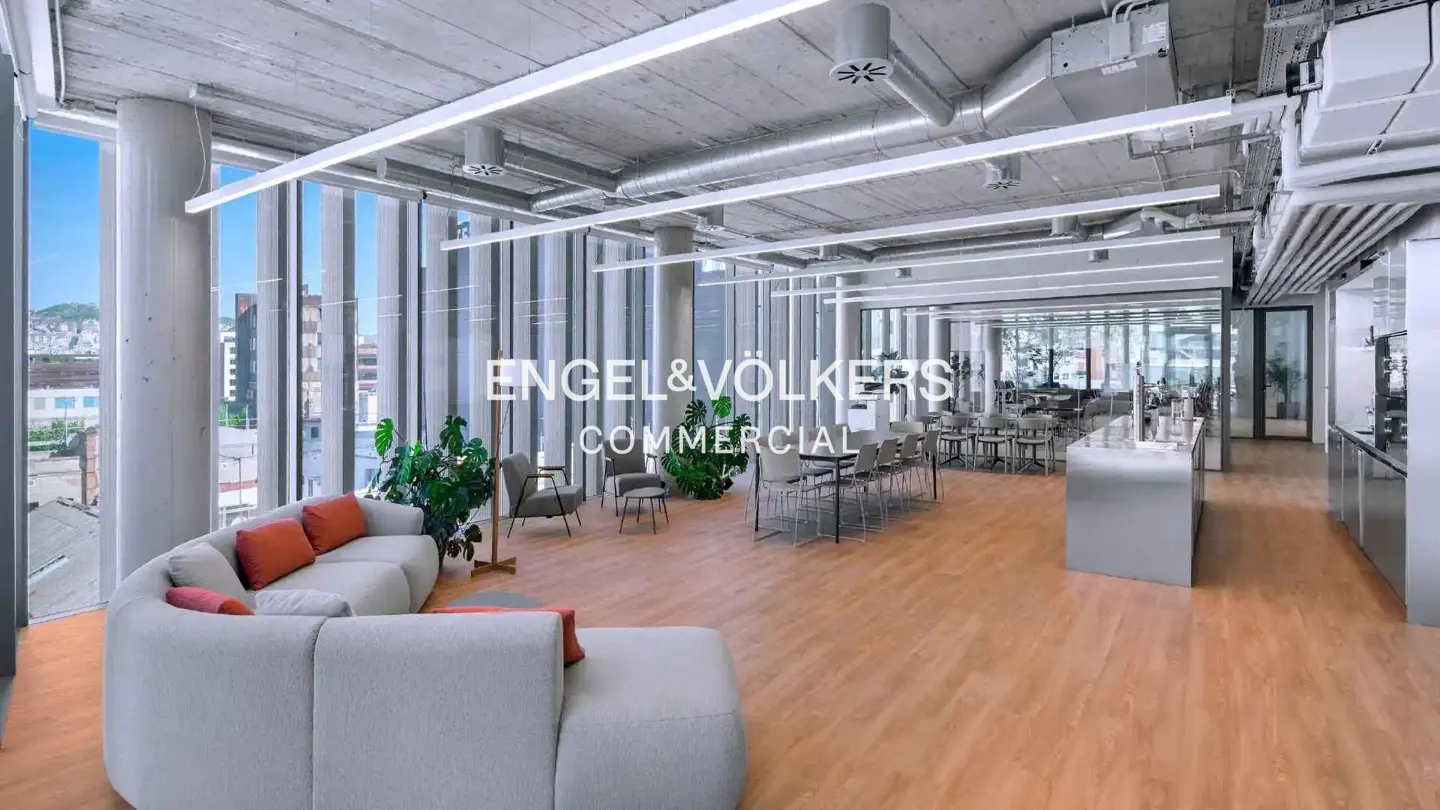 Engel & Völkers commercial space with a white sofa, orange pillows, wood floors, and large windows.