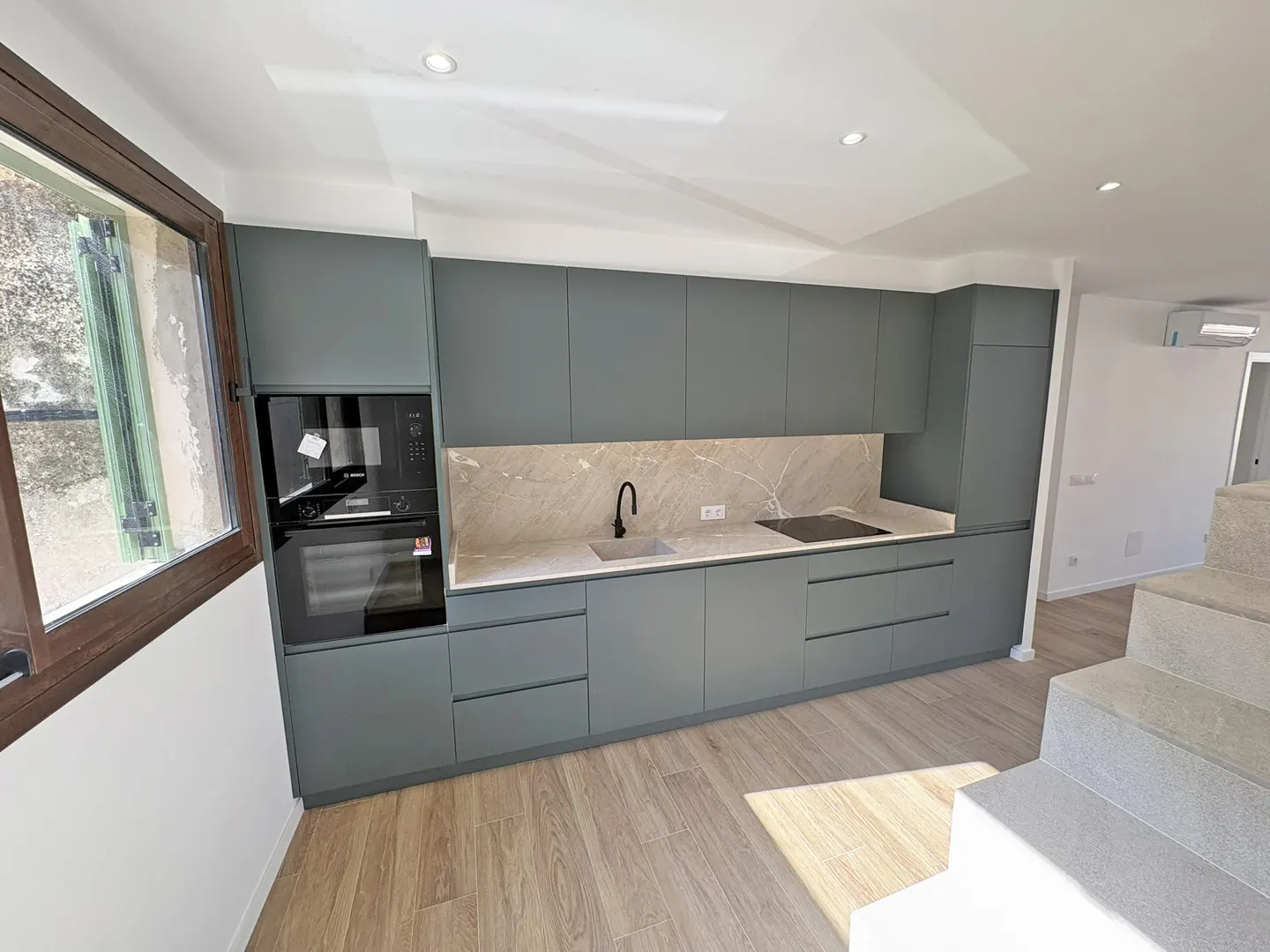 Modern kitchen with gray cabinets, marble backsplash, black faucet, and wood floors. Stairs lead to another level.