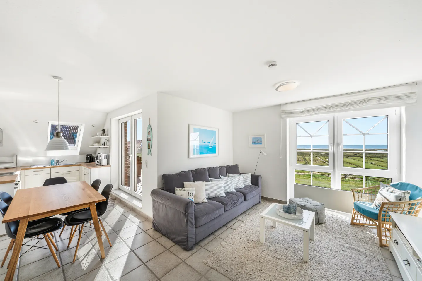 Bright, open-concept living space with a gray sofa, wood table, and a view of the ocean through a large window.