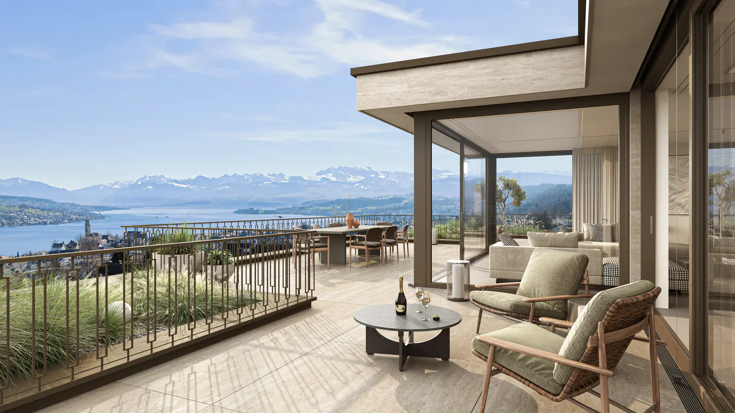 Luxury apartment balcony with lake and mountain views. Table, chairs, wine, and greenery create an inviting outdoor space.