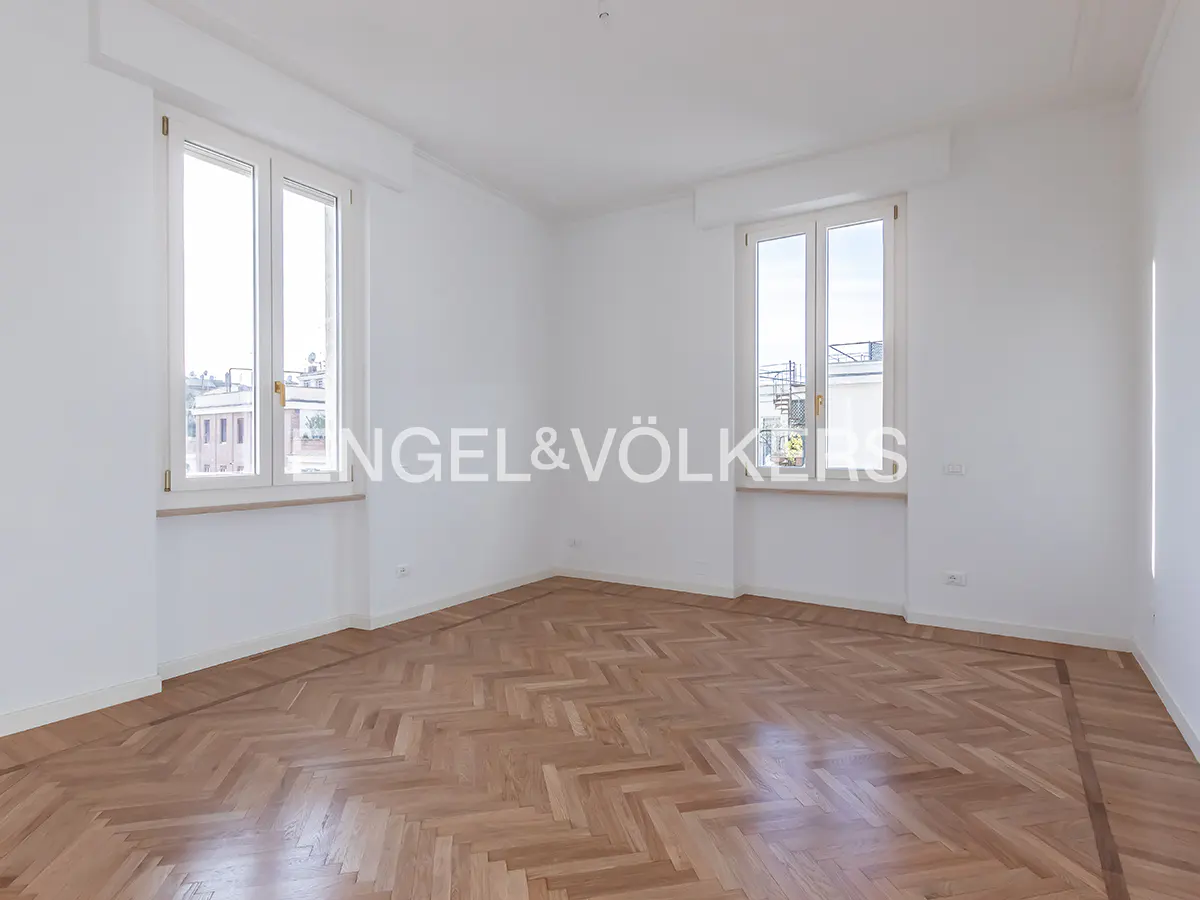 Empty white room with herringbone wood floor, two windows, and Engel & Völkers logo.
