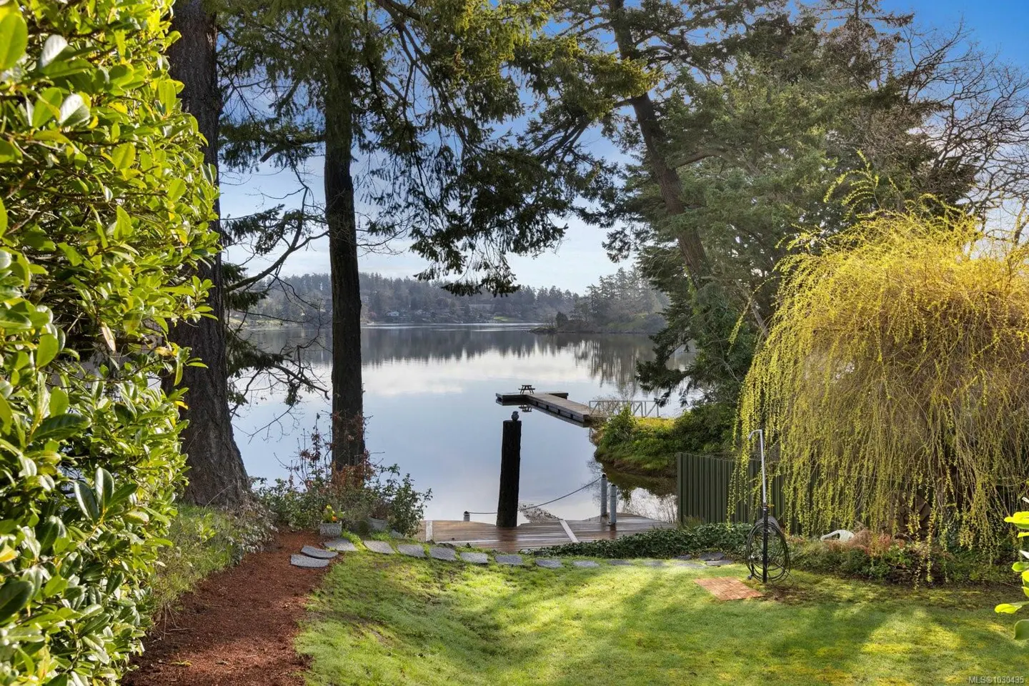 Waterfront property with a dock on a calm lake, framed by green trees and lawn.