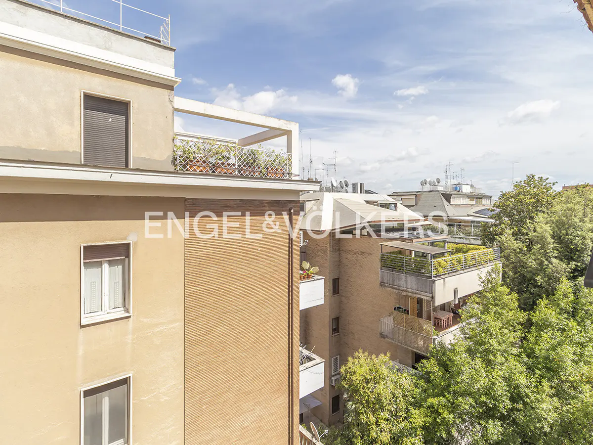 View of city buildings with balconies and trees under a blue sky with clouds. Engel & Volkers logo is visible on the building.