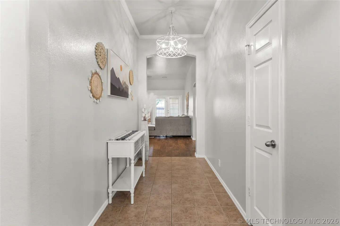 Bright hallway with tile floor, white console table, wall art, and a modern chandelier leading to a living room.