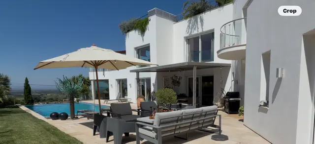 Modern white house with a pool, patio furniture, and a large umbrella on a sunny day.