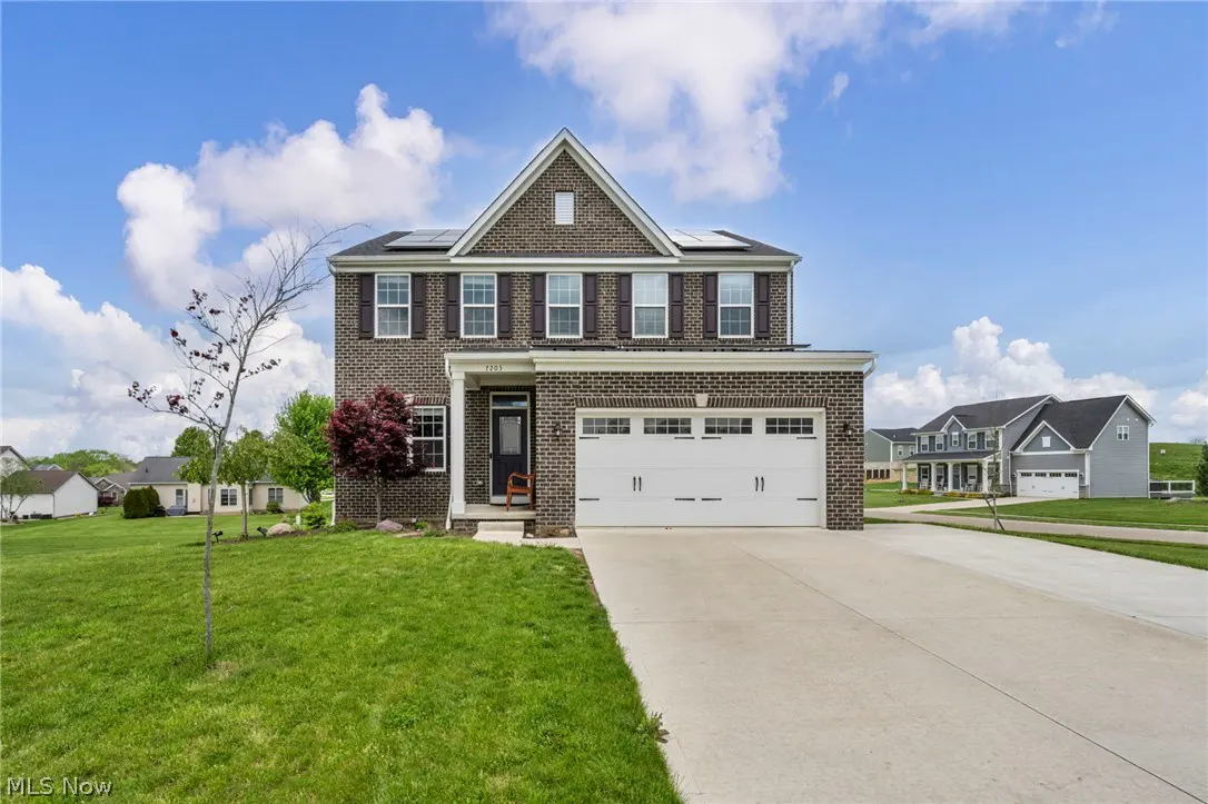 Two-story brick house with a white garage door, black shutters, and a green lawn under a blue sky.