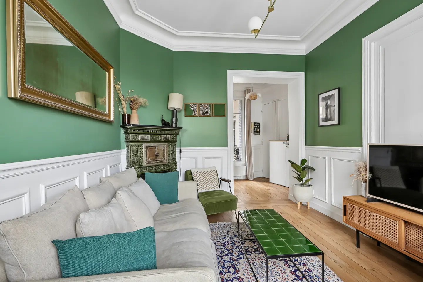 A living room with green walls, a white sofa with teal pillows, and a green tiled coffee table on a patterned rug.