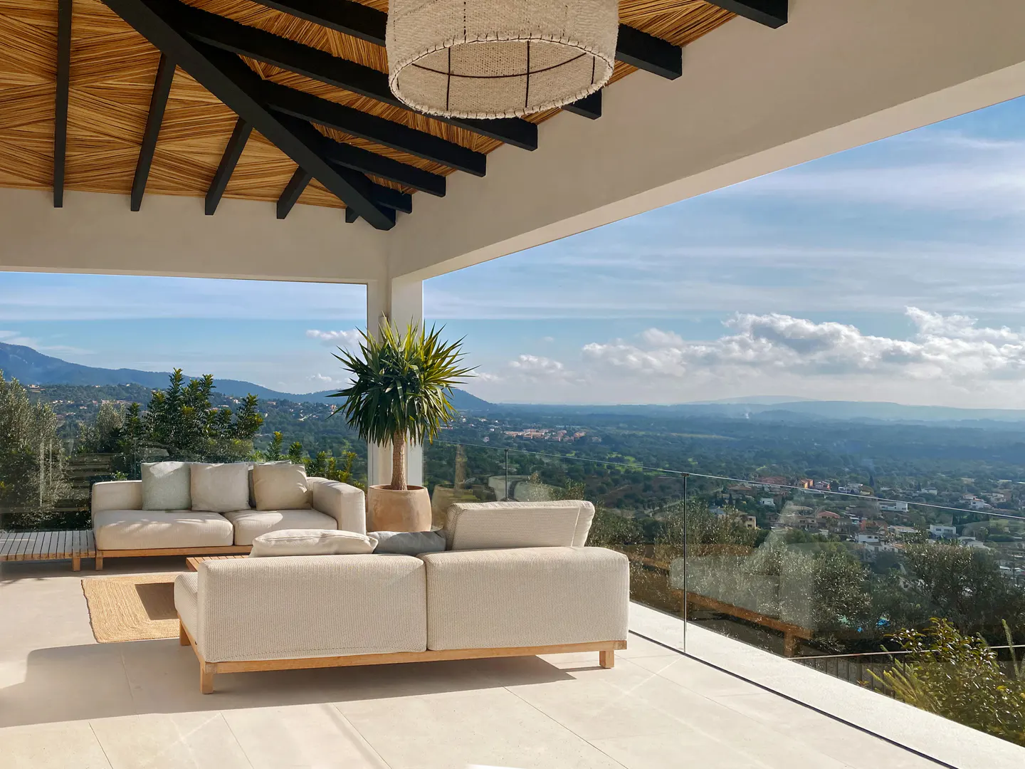 A bright, airy patio with white sofas, a potted plant, and a view of rolling hills under a blue sky.