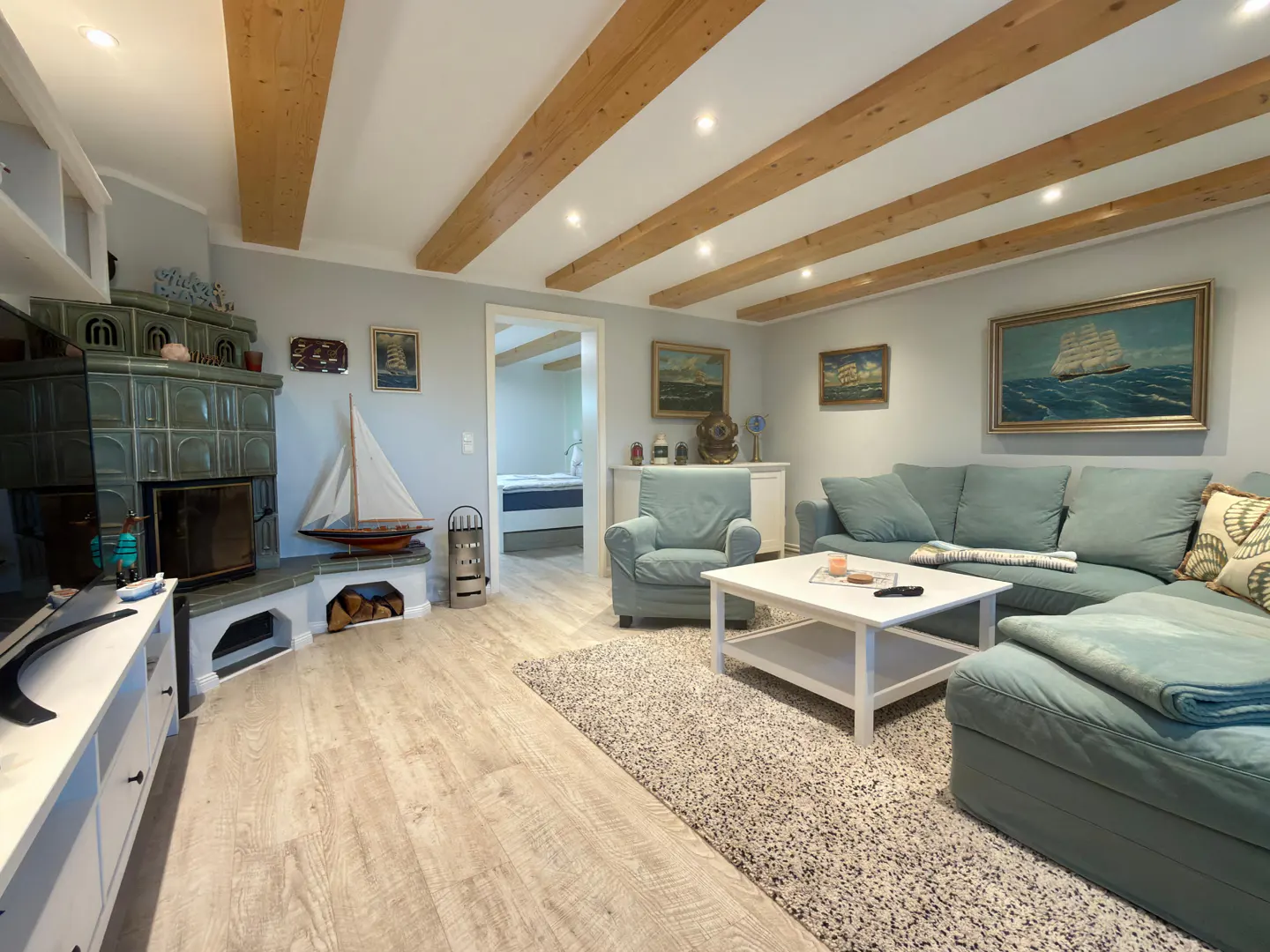 Living room with light blue walls, wooden ceiling beams, a blue sofa, and a tiled fireplace.