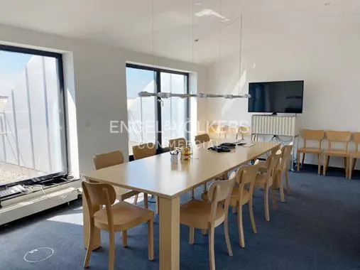 Bright conference room with a long table, chairs, and a TV. Large windows let in natural light. Engel & Volkers logo visible.