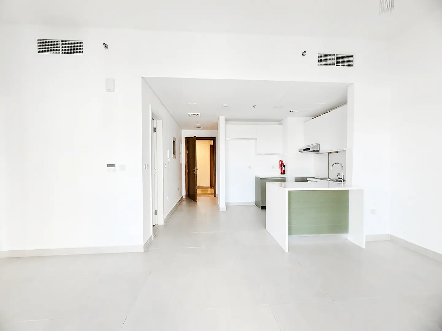 Modern open-plan apartment with white walls, light tile floors, and a kitchen featuring white cabinets and a green island.