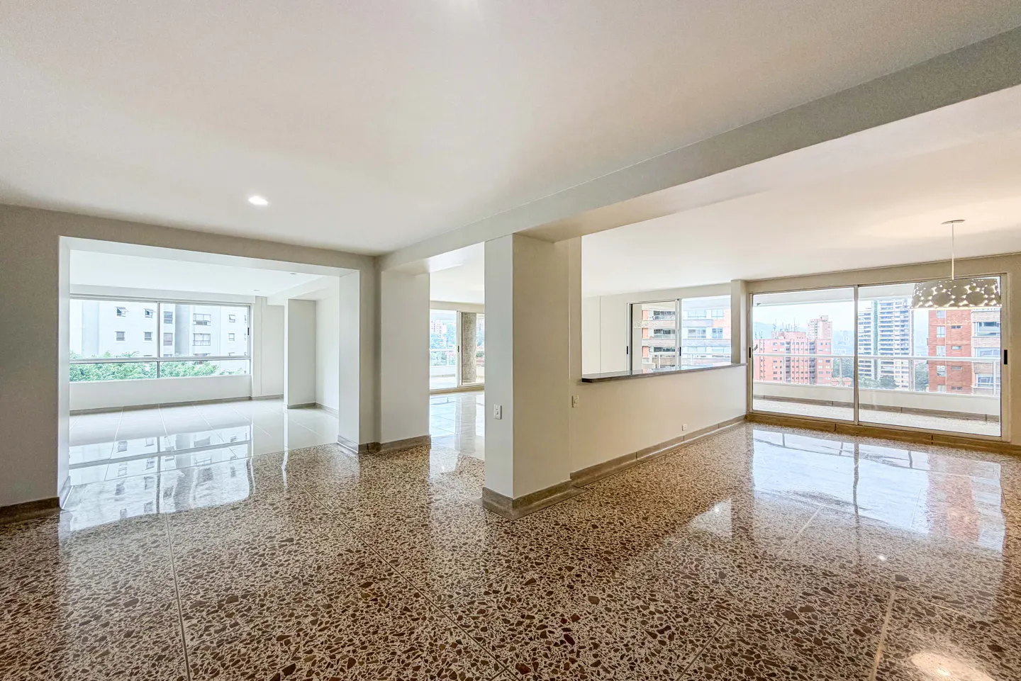 Bright, empty apartment with terrazzo floors and white walls. Large windows offer city views.