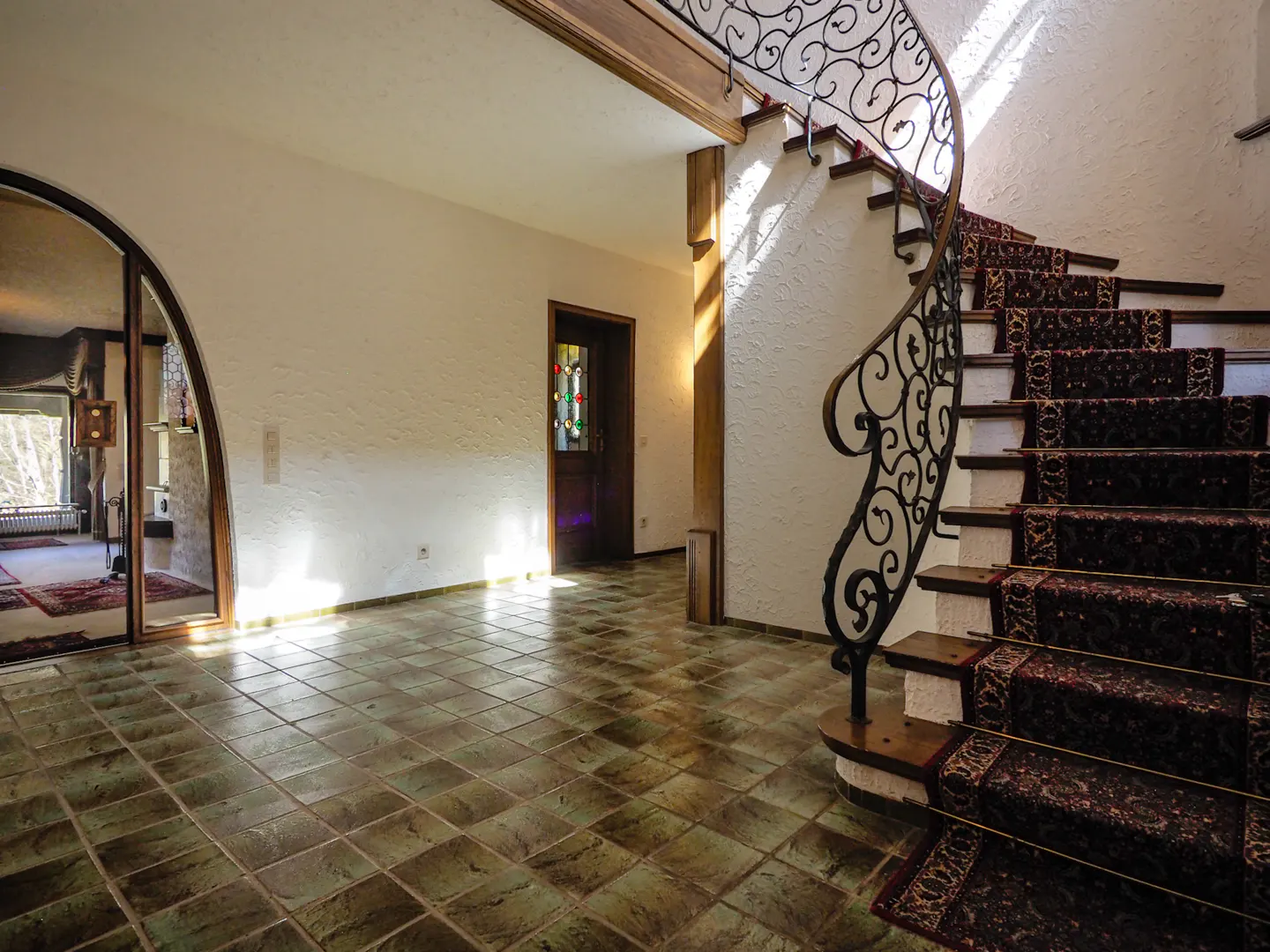 Foyer with tile floor, white walls, and a curved staircase with a black wrought iron railing and patterned carpet. A stained glass door is visible.