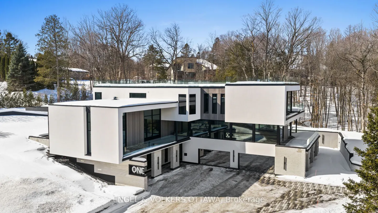 Modern white house with black trim and large windows, surrounded by snow and bare trees under a blue sky.