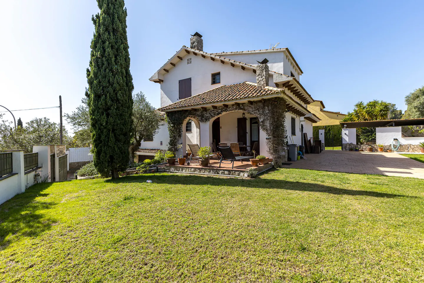 Exterior of a two-story white house with a stone chimney and a tile roof, surrounded by a green lawn and trees.